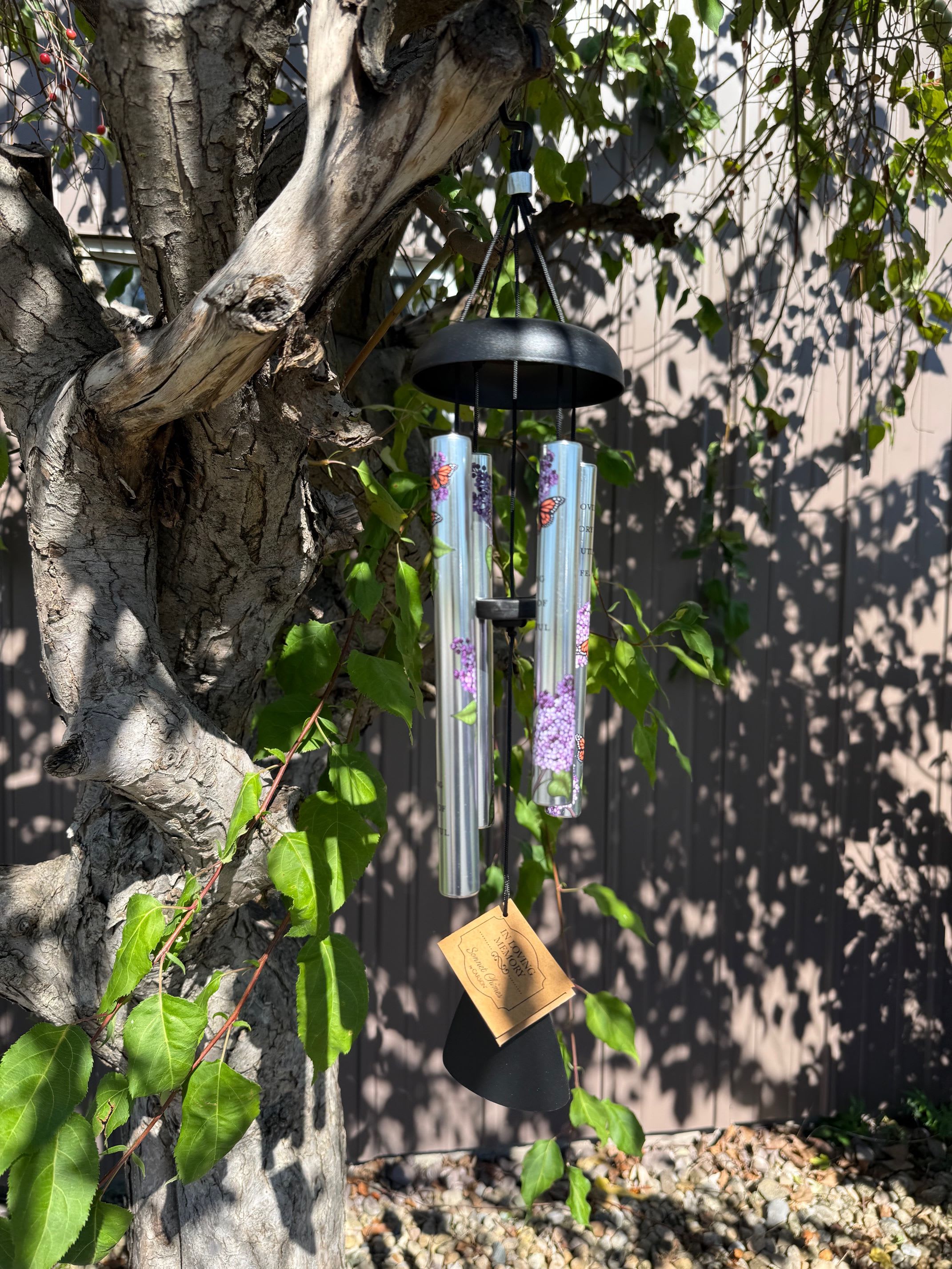 Black wind chime hanging from a tree branch outdoors