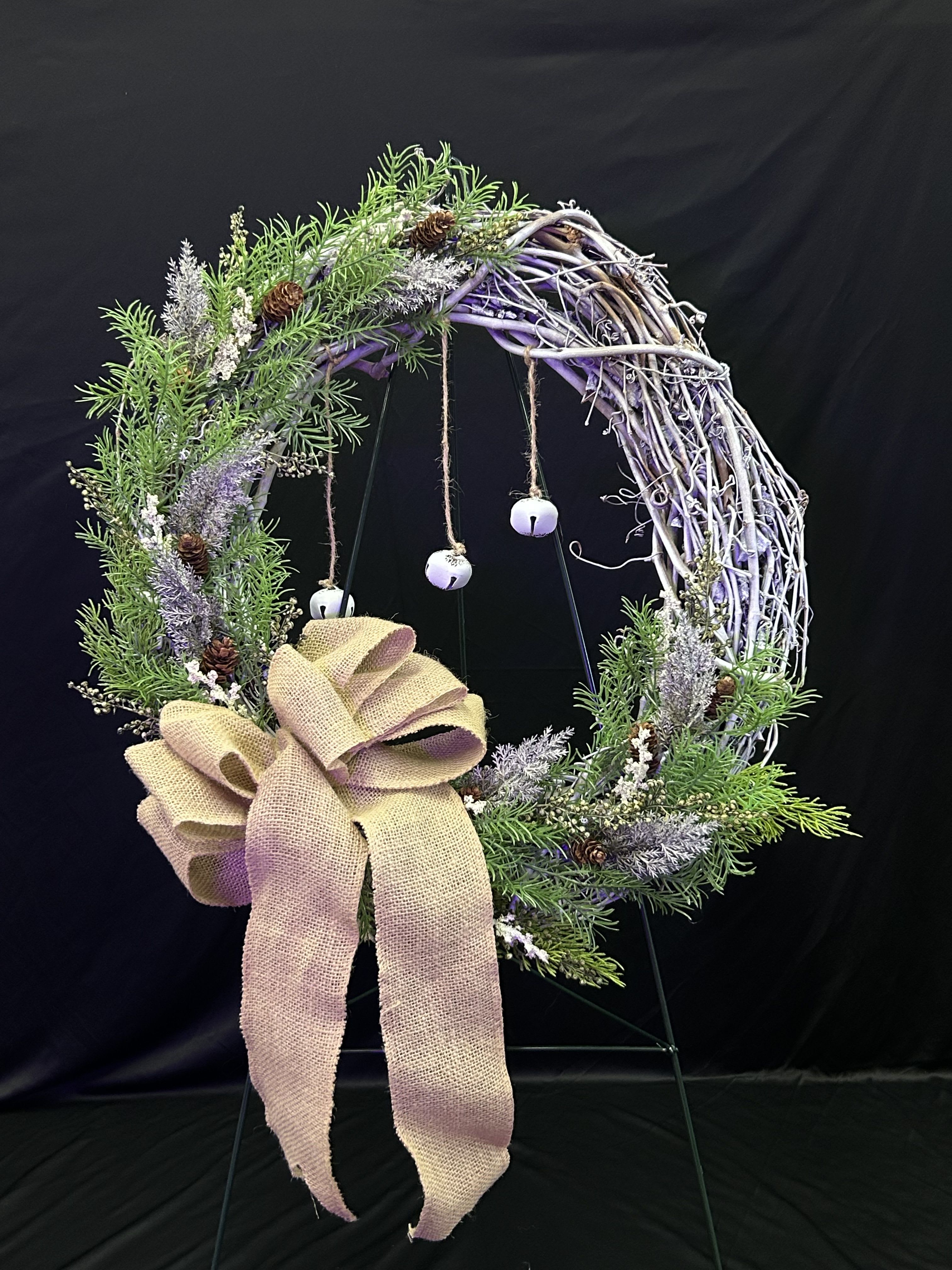 Rustic wreath with greenery, pinecones, and a burlap bow on a stand