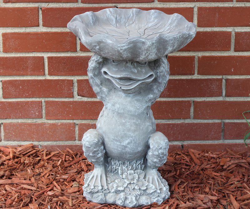 Gray garden frog statue against a brick wall