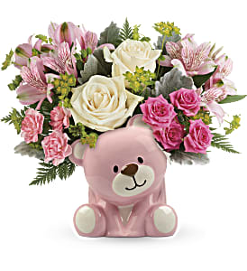 Pink teddy bear holding a bouquet of pink and white flowers