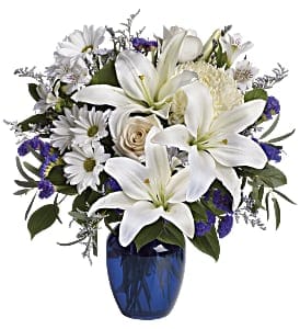 White lilies and daisies arranged in a blue glass vase