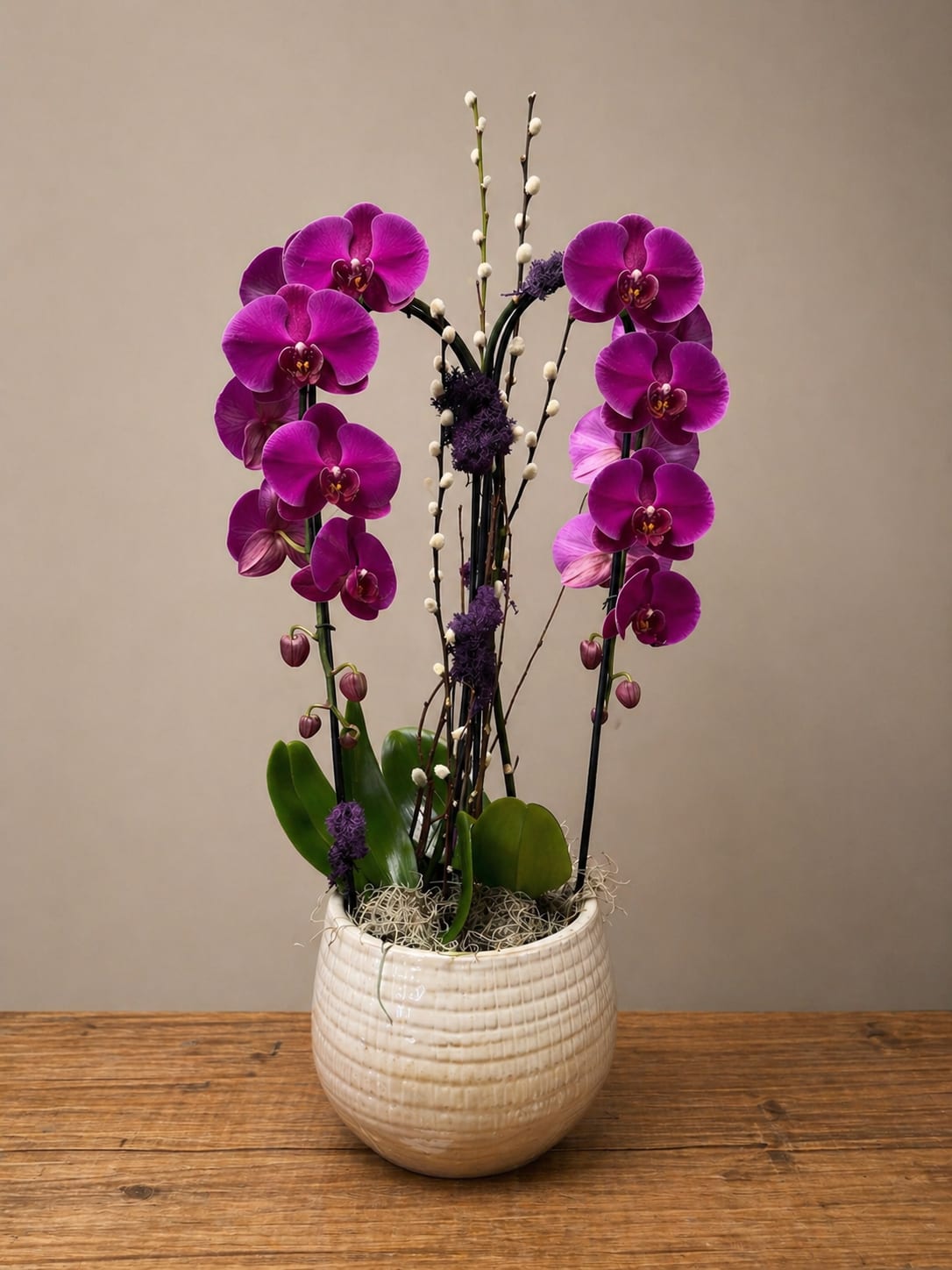 Royal Orchid  - A breathtaking arrangement of vibrant fuchsia phalaenopsis orchids, artfully designed with natural branches and textured accents in a modern ceramic vessel. This elevated composition offers bold color, graceful movement, and refined sophistication—perfect for making an unforgettable statement in any space.