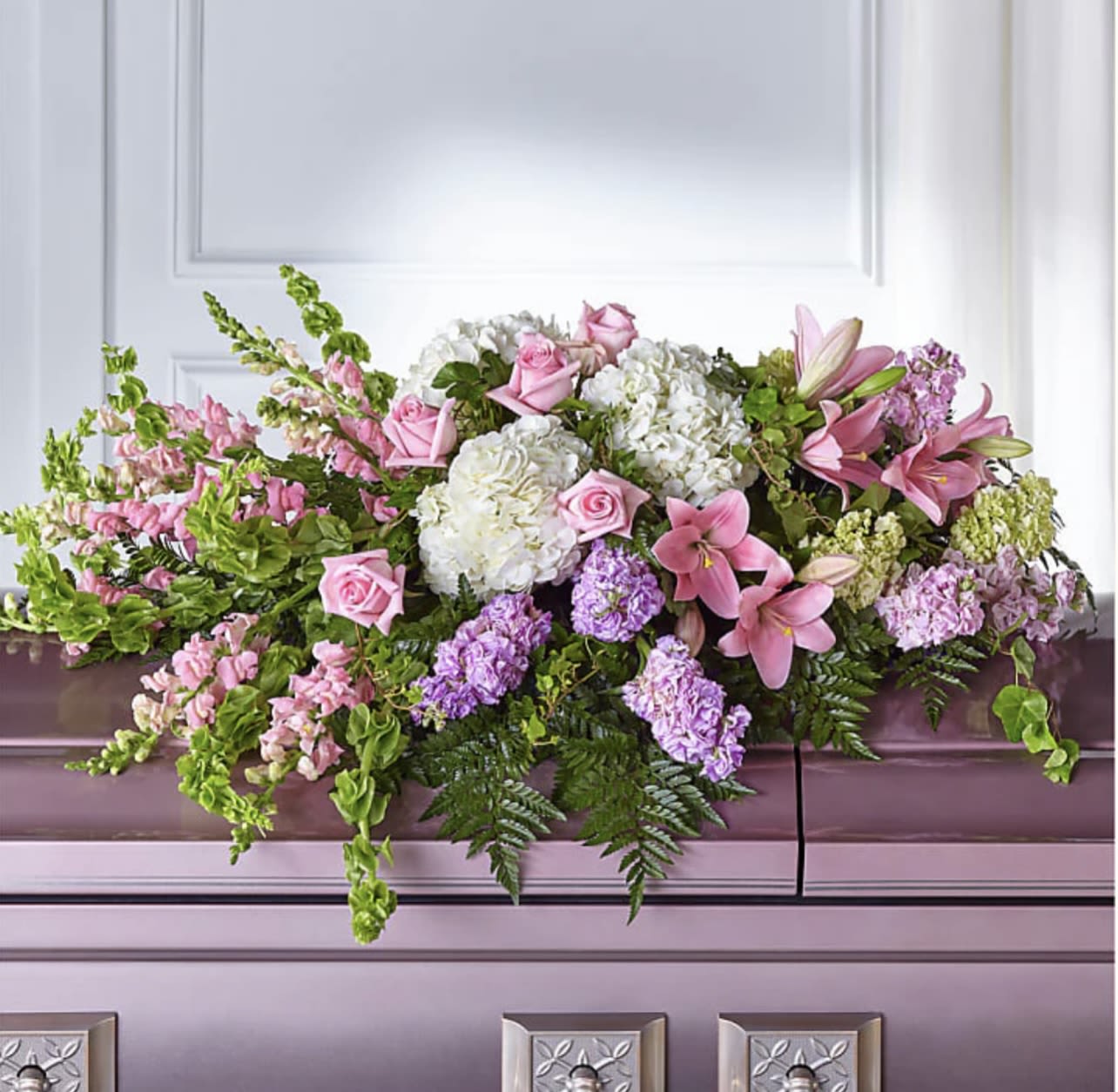 Pink and white floral casket spray with lilies, roses, and hydrangeas