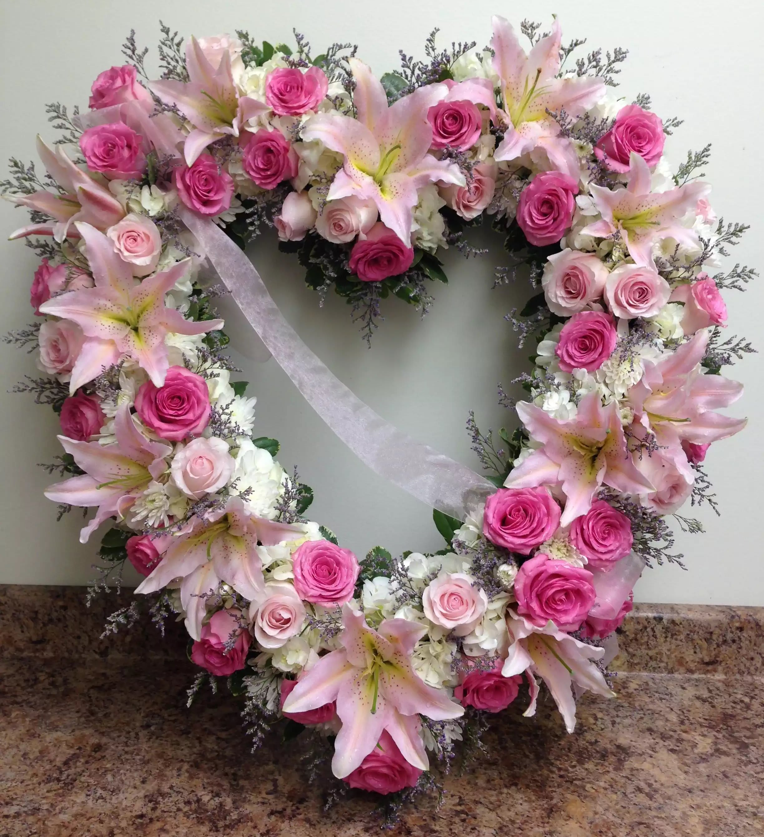 Heart-shaped wreath of pink roses and lilies with a white ribbon
