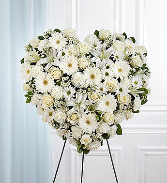 All White Mixed Flower Standing Heart Spray - It’s the purity of love that keeps us going when someone we care about is taken from us. This loving sentiment is best captured with our grand, heart-shaped arrangement in pure and timeless white. Handcrafted by our caring florists using a medley of pristine white blooms, it’s a beautiful tribute best suited for the funeral services.  All-white heart-shaped arrangement of roses, hybrid lilies, Gerbera daisies, carnations, daisy poms, waxflower and monte casino; accented with baby’s breath and soft, lush greenery Arrangement is designed on an easel Measures approximately 26"H x 28"W without easel Appropriate for the funeral home Our florists use only the freshest flowers available, so colors and varieties may vary