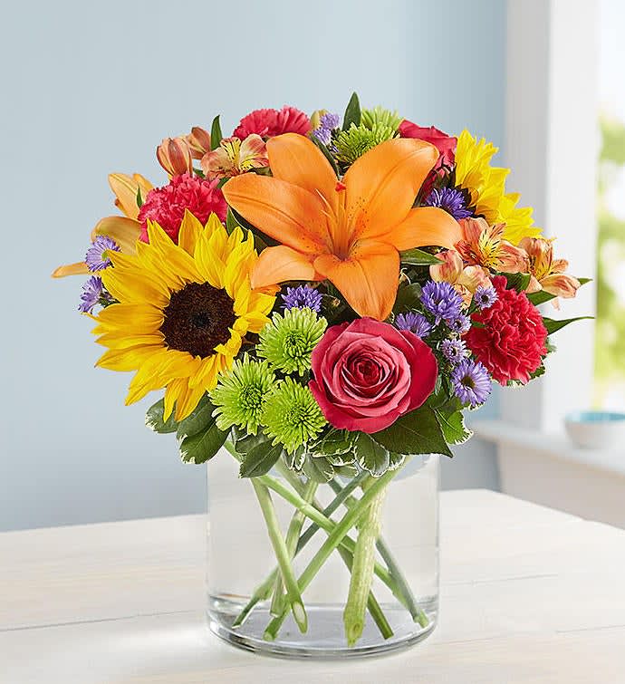 Bright mixed bouquet with sunflowers, orange lily, pink rose, and colorful blooms in a clear glass vase