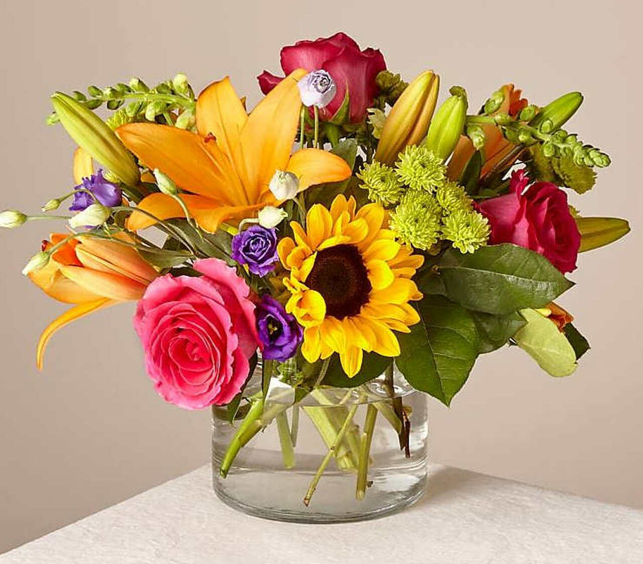 Mixed bouquet of roses, lilies, and a sunflower in a glass vase