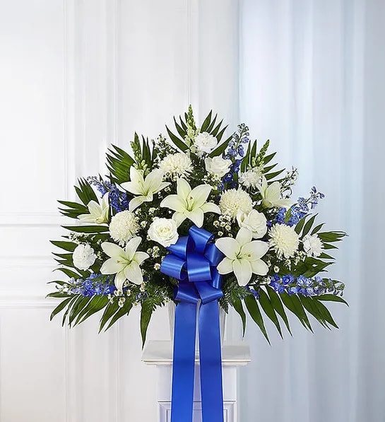 White floral standing spray with a blue ribbon on a pedestal