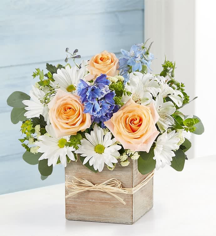 Bouquet of peach roses, white daisies, and blue flowers in a wooden box