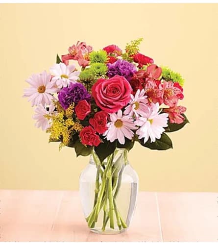 Mixed bouquet of pink, red, purple, and white flowers in a clear glass vase