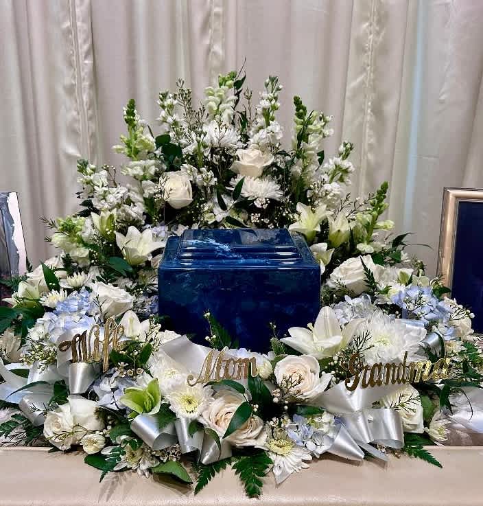 White floral funeral arrangement surrounding a blue urn with memorial name signs
