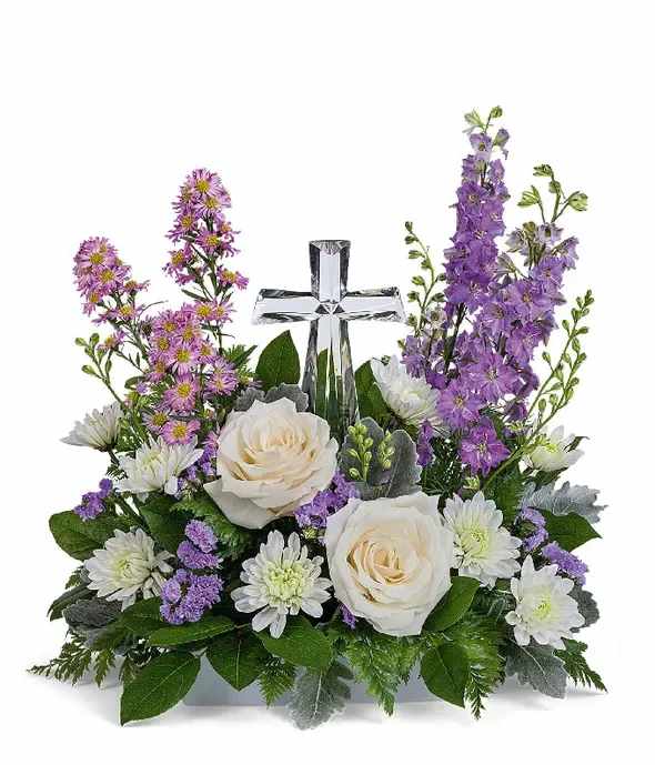 White roses and purple flowers arranged around a clear glass cross