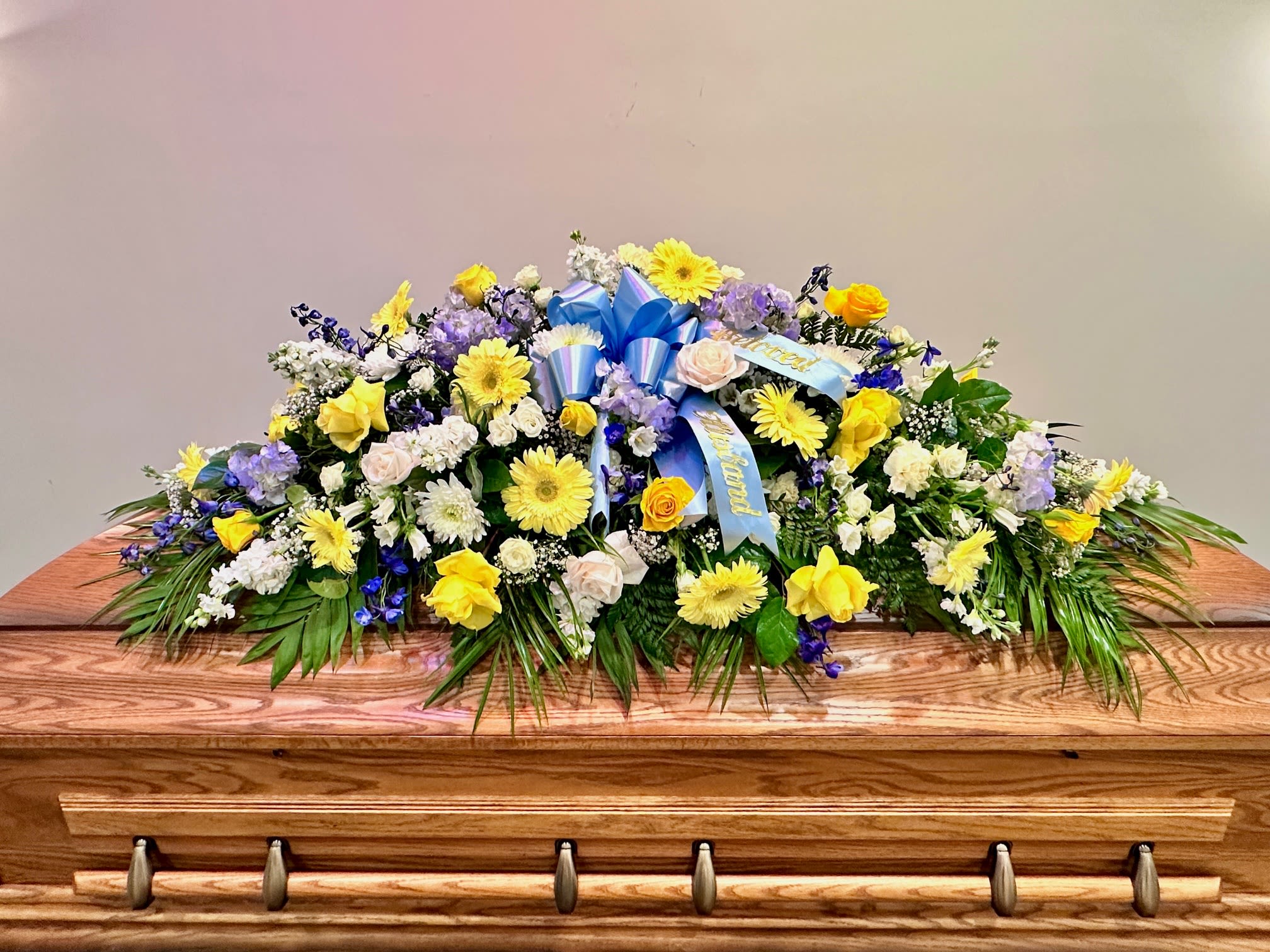 Large floral casket spray with yellow, white, and purple flowers
