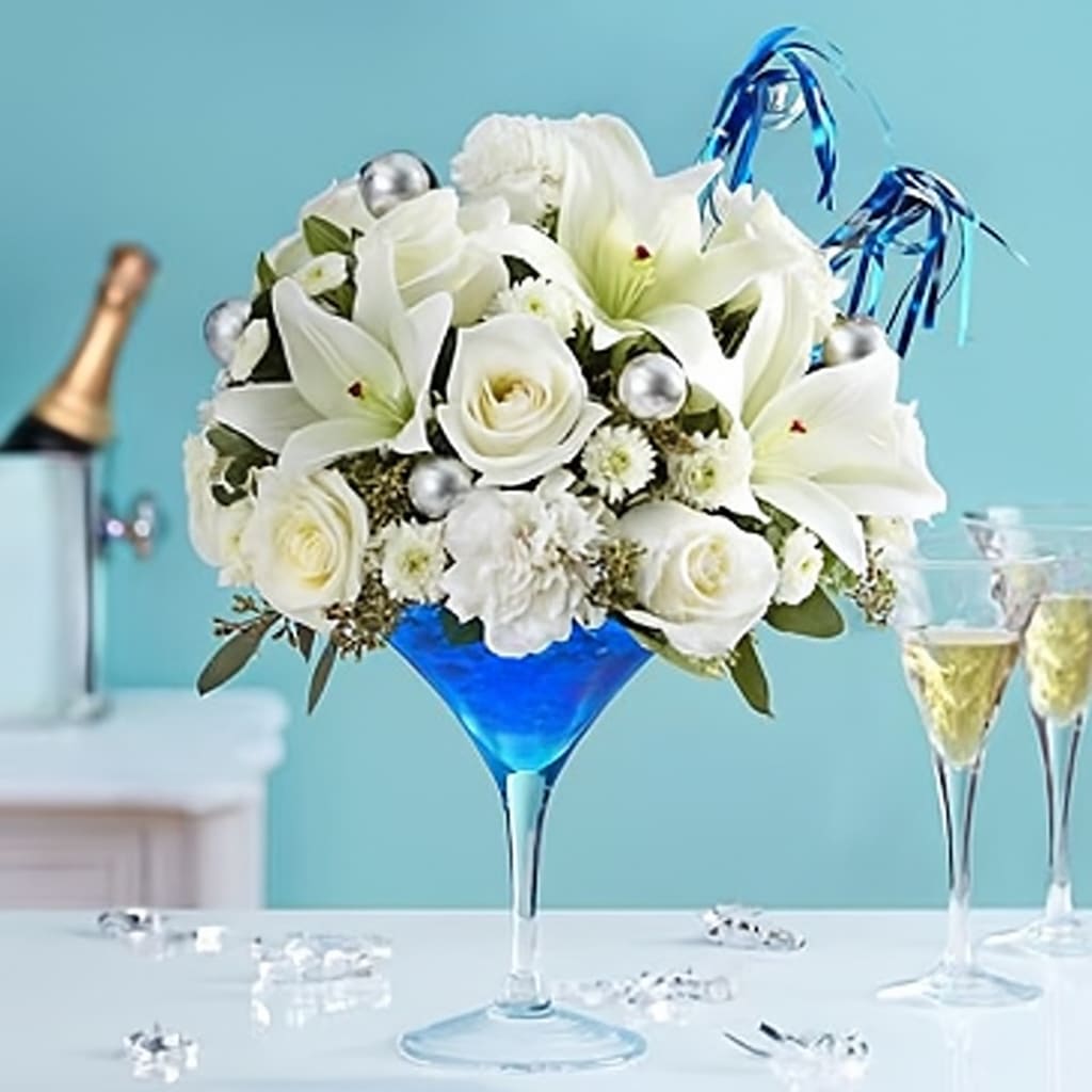 Cheers to the New Year - EXCLUSIVE Ring in the new year with our famous cocktail-inspired creation! A striking white mix of blooms mingle inside an oversized margarita glass, complete with blue &amp; white party horns and shimmering silver ornaments. This spirited arrangement is the perfect centerpiece for every New Year’s celebration.  All-around arrangement with white roses, Asiatic lilies, carnations and button poms; variegated pittosporum and seeded eucalyptus; accented with blue &amp; white party horns and silver ornament balls Lilies may arrive in bud form and will open to full beauty over the next 2-3 days Our florists select the freshest flowers available, so colors and varieties may vary due to local availability Artistically designed in a 10"H reusable, food-safe acrylic margarita glass filled with sapphire blue decorative gel