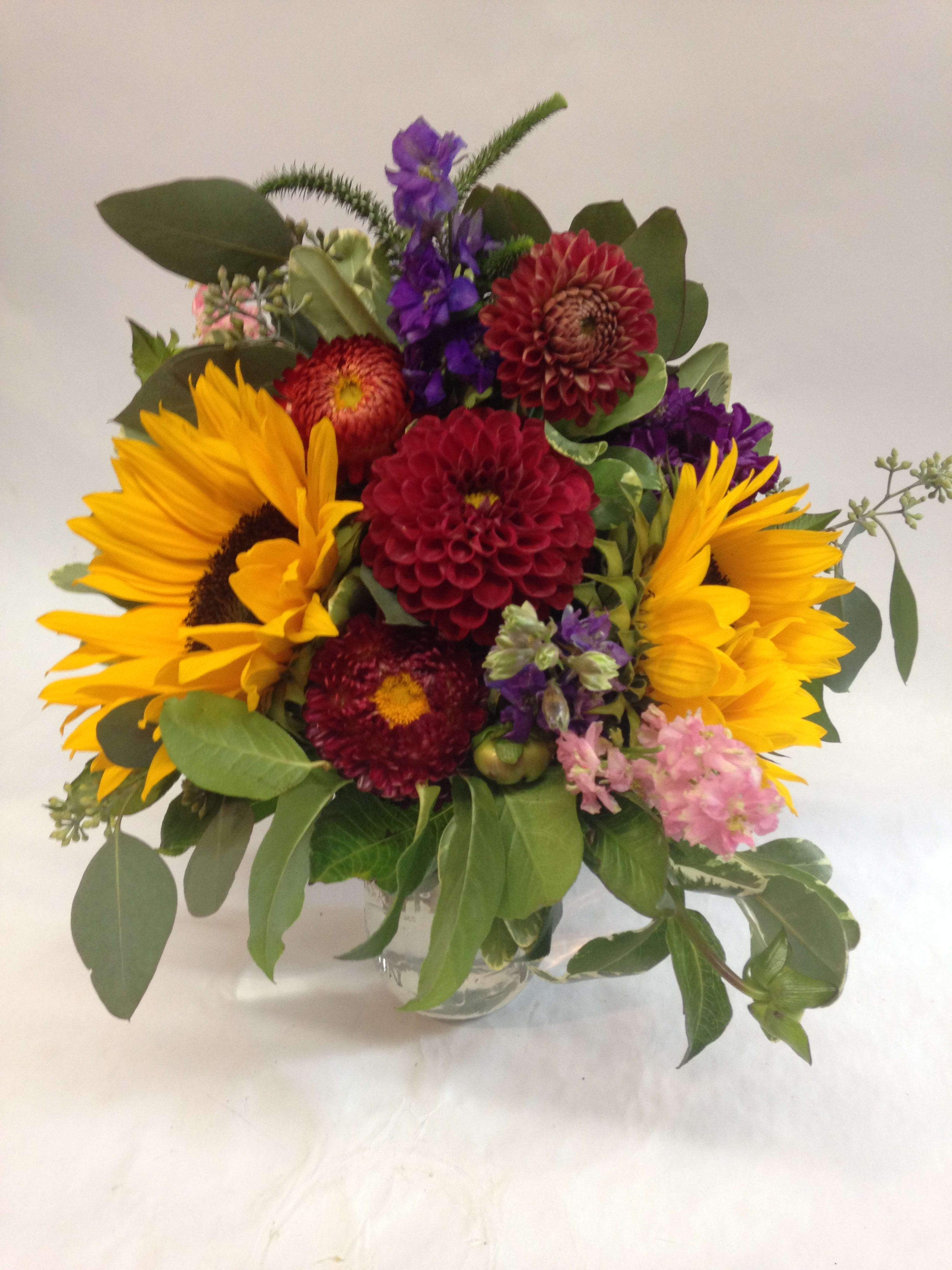 Mixed bouquet with sunflowers, purple blooms, and red dahlias in a glass vase