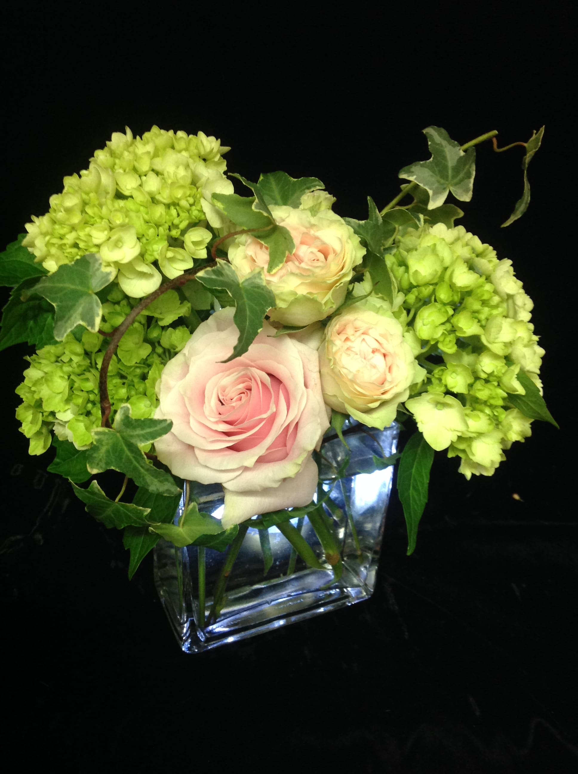Compact arrangement of pale pink roses and green hydrangeas in a clear glass cube vase.