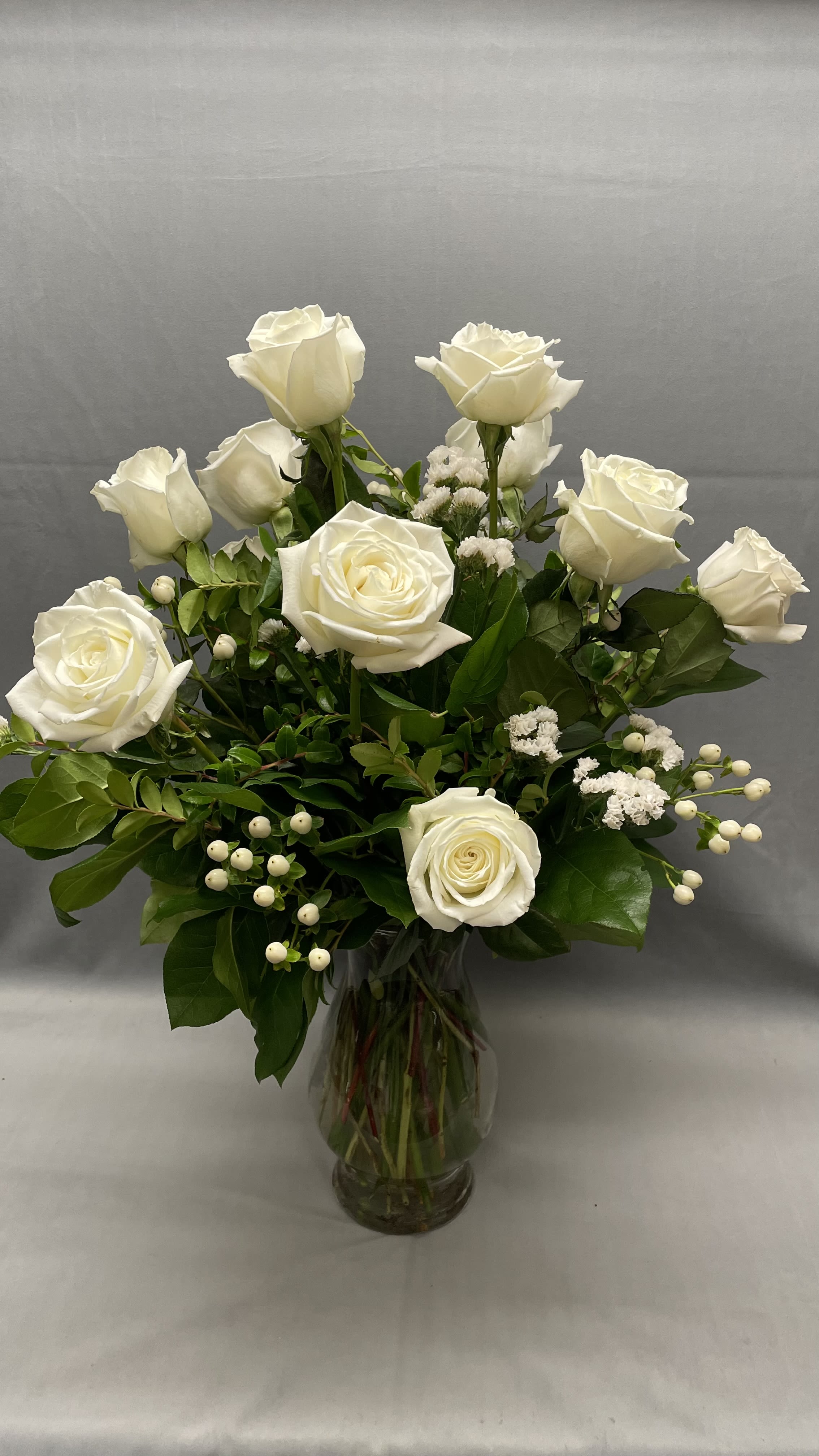 Tall arrangement of white roses and white filler flowers in a clear glass vase