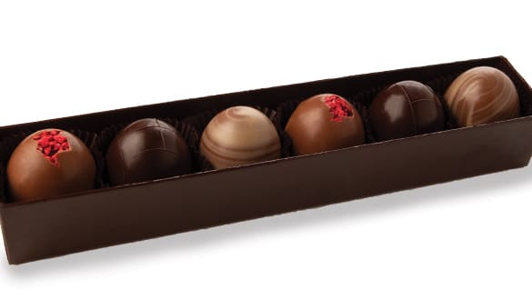 Row of six assorted chocolate truffles in a long dark brown box