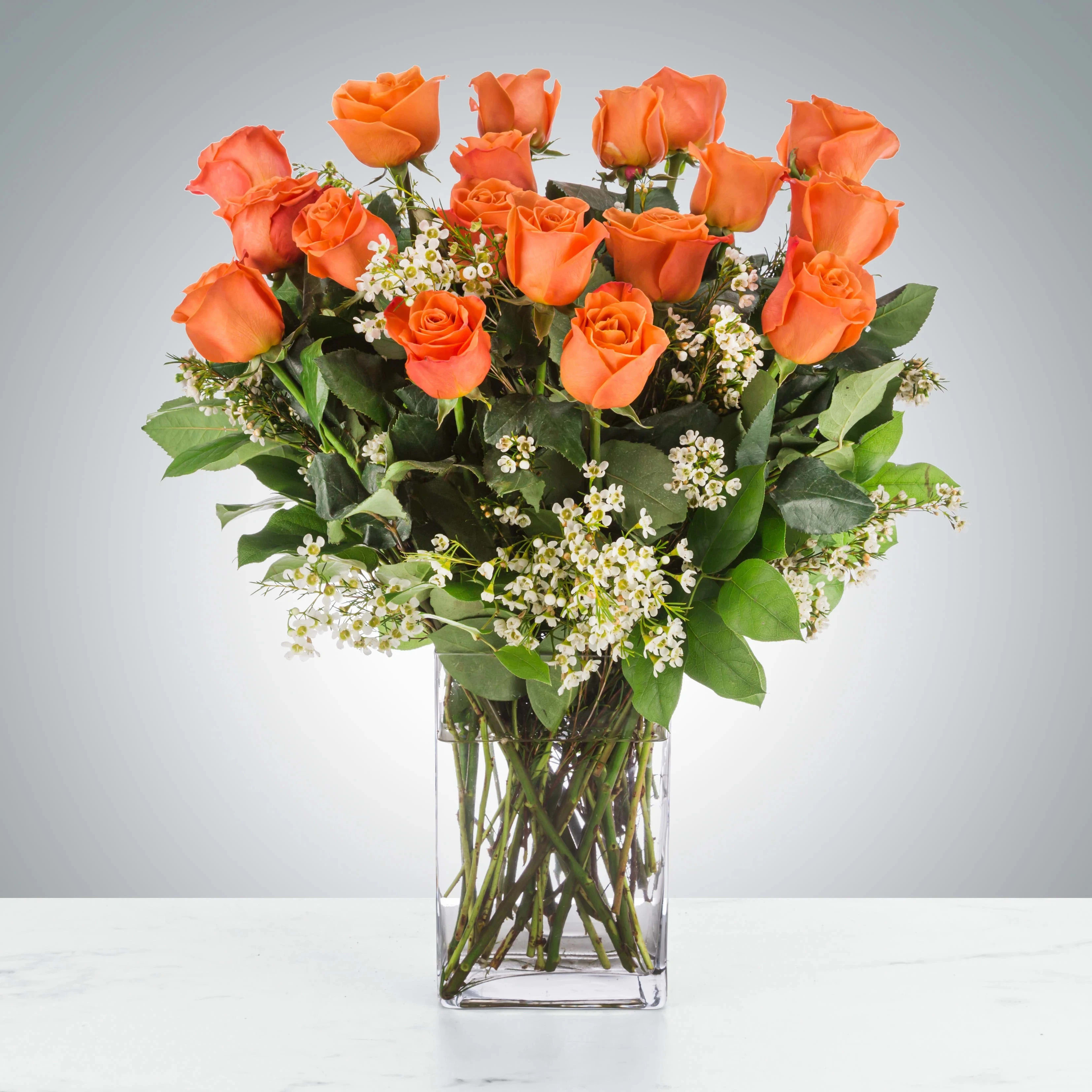 Tall arrangement of orange roses with small white blooms in a clear glass vase