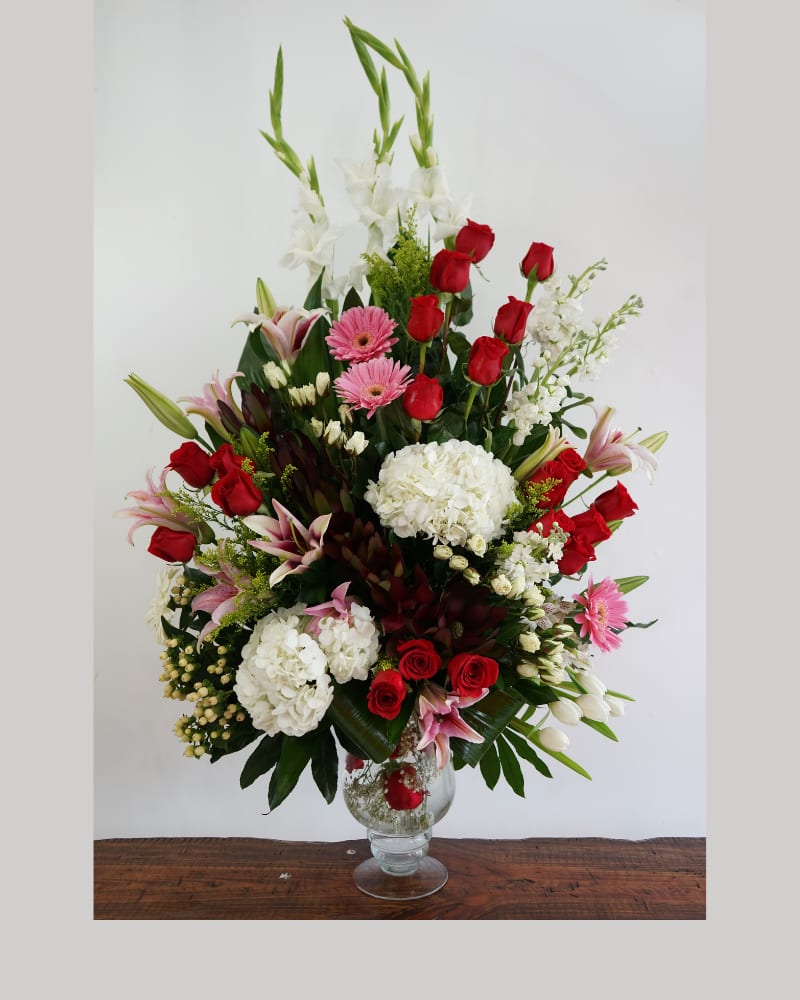 Tall mixed arrangement of red roses, white hydrangeas, pink lilies and gerberas in a clear glass vase