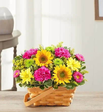 Bright basket arrangement of yellow sunflowers, pink carnations, and yellow and green mums.
