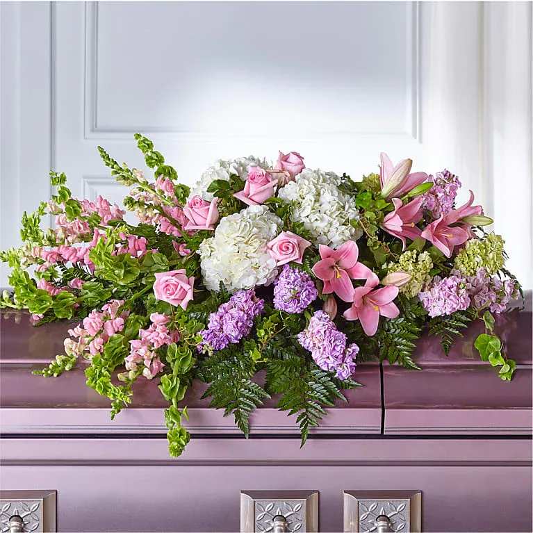 Pastel pink and white casket spray with roses, lilies, hydrangeas and lavender flowers on a mauve casket