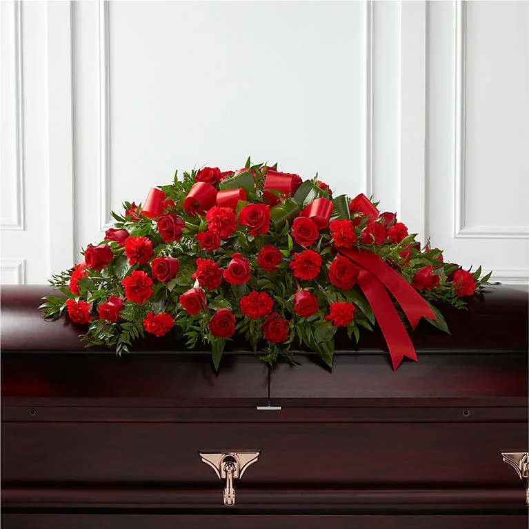 Red roses and carnations casket spray with red ribbon on a dark wood casket