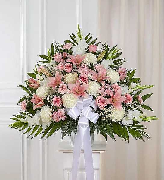 Large pink and white floral arrangement with a white bow displayed on a pedestal