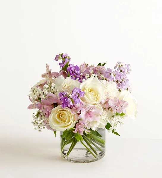 Low glass vase arrangement with cream roses, white blooms, and soft pink and lavender flowers