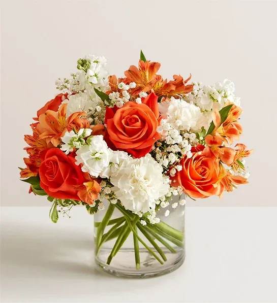 Compact bouquet of orange roses and white flowers in a clear glass vase