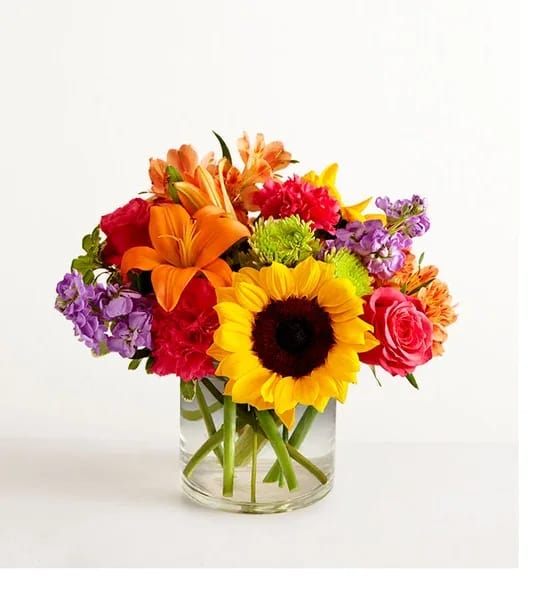 Bright mixed bouquet with sunflower, orange lilies, and pink blooms in a clear glass vase