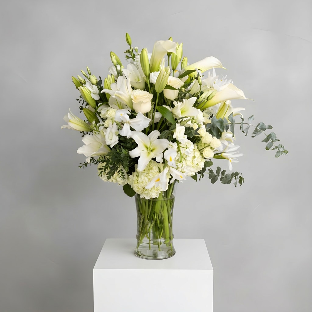 Eternal Grace Tribute - Elegant, serene, and timeless, Eternal Grace Tribute is a luxurious all-white arrangement featuring premium lilies, roses, calla lilies, hydrangea, snapdragons, and delicate seasonal blooms accented with fresh eucalyptus and lush greenery. Designed in a tall clear glass vase, this sophisticated piece conveys peace, purity, and heartfelt sentiment, making it ideal for sympathy services, memorials, churches, elegant events, or meaningful expressions of love and remembrance.