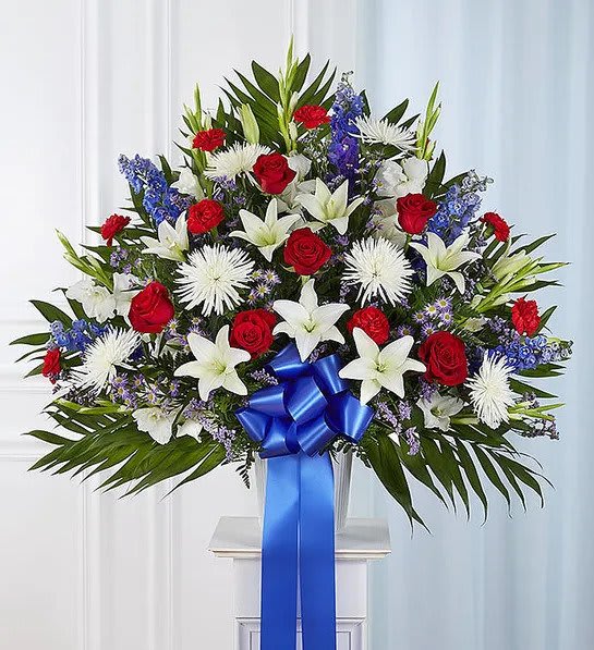 Heartfelt Sympathies™ Red, White and Blue Standing Basket - The love they showed for their country is as deep as the love felt by those mourning their loss. Meticulously crafted by our expert florists to honor a proud veteran who has passed away, our majestic standing basket arrangement is filled with lush blooms in patriotic red, white and blue, creating a fitting final tribute for the funeral services.