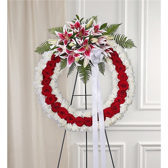 Love Forever™ Wreath - There’s something so meaningful about the circular design of a wreath for honoring a love that will live on forever. Our large tribute wreath is a truly impressive arrangement of rich red and pristine white blooms. It’s uniquely designed with a cluster of fresh, pink lilies at the top that are beautifully accented with a bow and trailing ribbons. It’s a tribute that will leave a loving, lasting impression. Large standing wreath arrangement of Red roses, white carnations, Stargazer Lilies and assorted greenery; white bow with trailing ribbon Arrangement measures 35”H x 26” W (without stand) Arrives with standing easel; measures 66” H A grand display appropriate for the funeral or memorial service Our florists use only the freshest flowers available, so colors and varieties may vary due to local availability.  Add a Sympathy Banner to this arrangement! https://katyflowershop.com/katy-katy-flower-shop/sympathy-banner.html