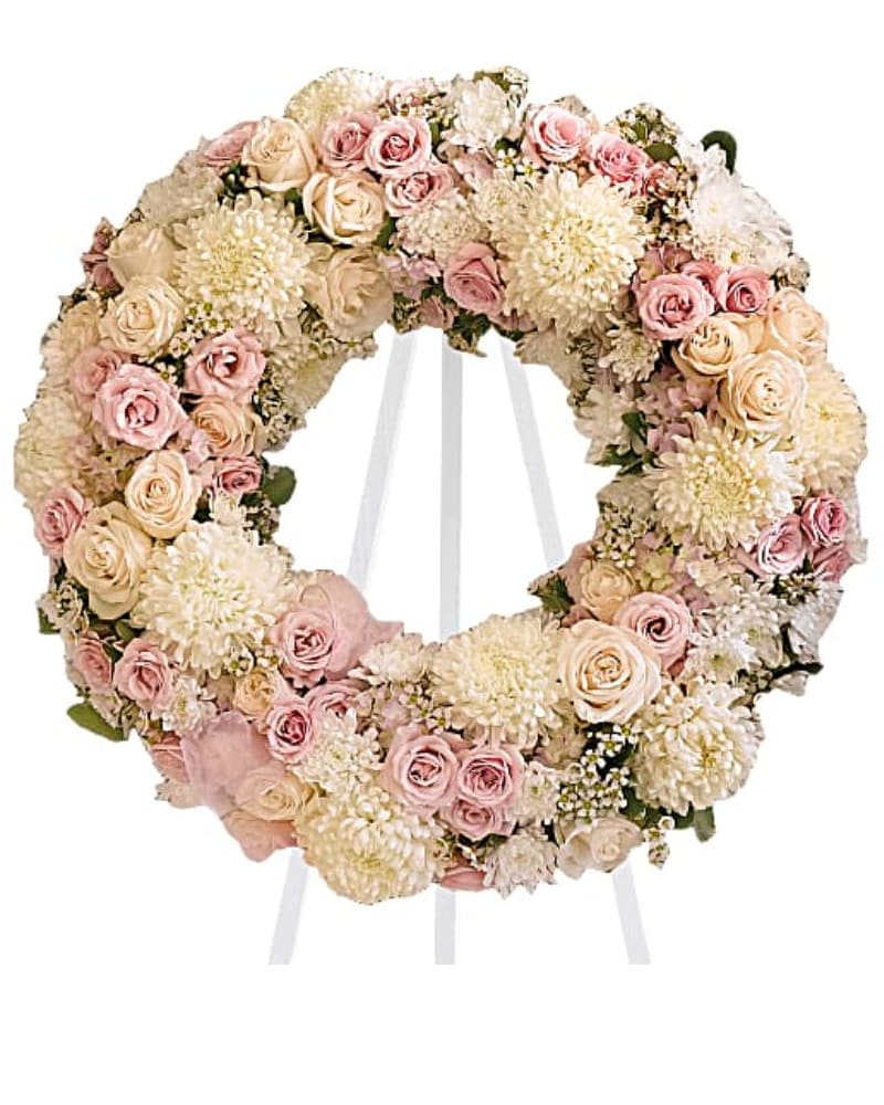 Peace Eternal Wreath - A pure and delicate expression of adoration. Accented with a sheer pink organza bow, this wreath of white, crème, and pale pink petals gently embraces loving memories, and offers solace and sweet thoughts at a time of loss. Lovely blooms such as crème and pink roses, pink hydrangea and white chrysanthemums are nestled together and accented with organza ribbon. A touching and feminine wreath, ideal for a memorial service.  Size of wreath without easel is 24 1/2" 