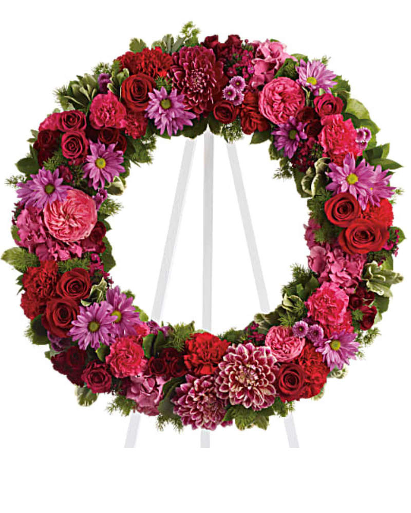 Infinite Love - Reminiscent of the rich jewel tones of an exquisite stained glass window, this lovely floral testament to the circle of life and love evokes beautiful memories even during the most difficult times. A standing wreath of stunning flowers such as hot pink roses and carnations, red roses, burgundy dahlias, dark pink Sweet William, lavender chrysanthemums and fresh greens.