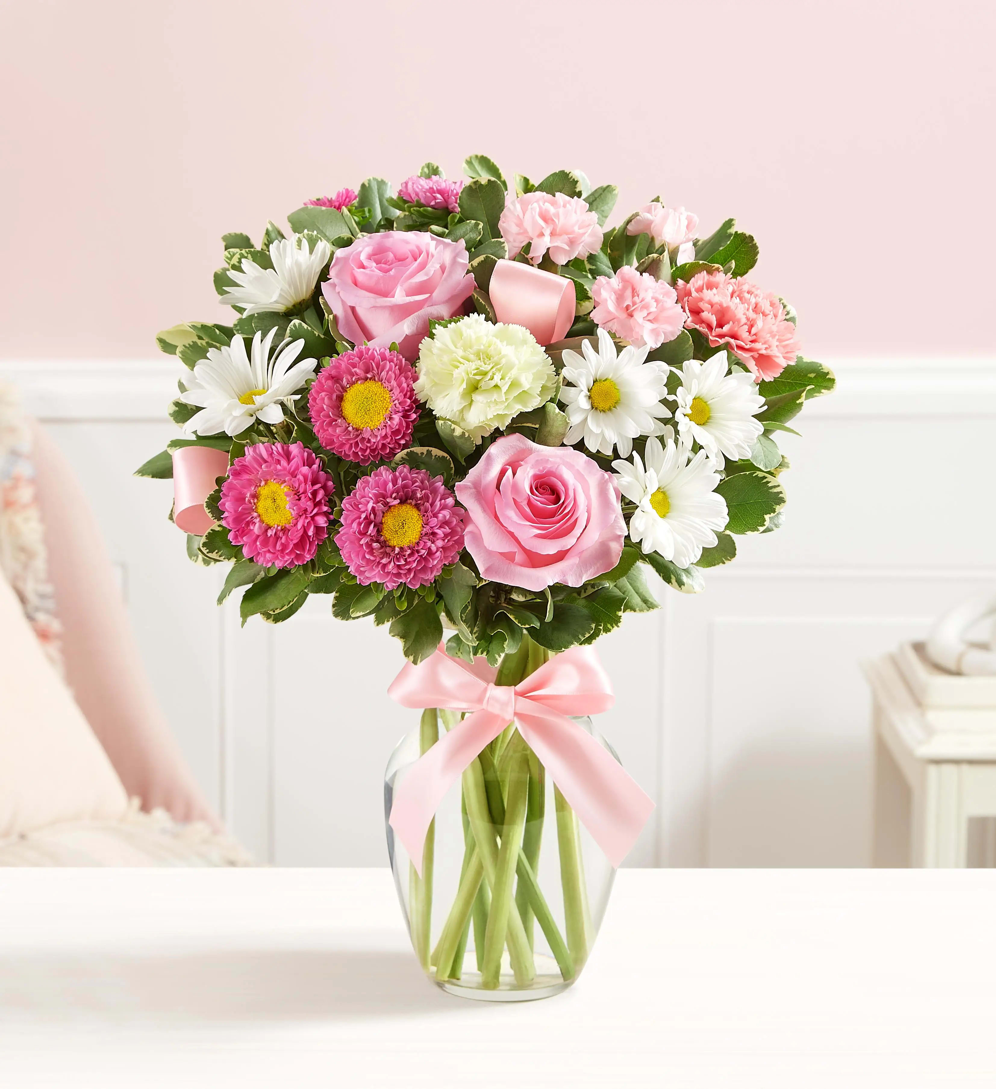Pink and white mixed bouquet in a clear glass vase with a pink ribbon
