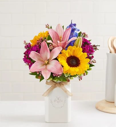 Bouquet of pink lilies, sunflowers, and purple flowers in a white vase