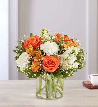 Orange roses and white flowers in a clear glass vase