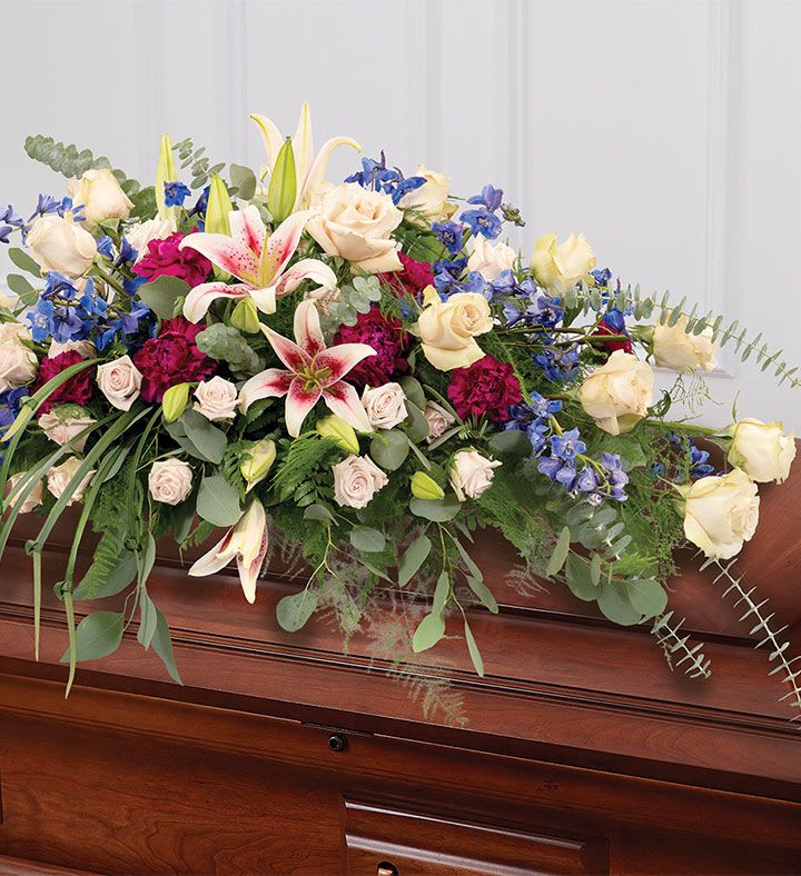 Casket spray with roses, lilies, and blue flowers