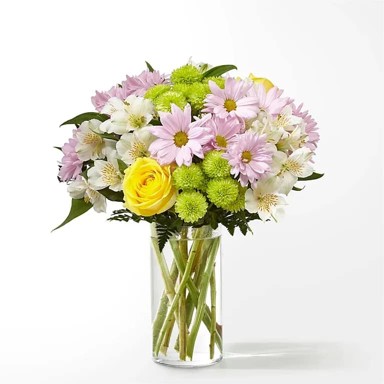 Mixed bouquet of yellow roses, pink daisies, green mums and white alstroemeria in a clear glass vase