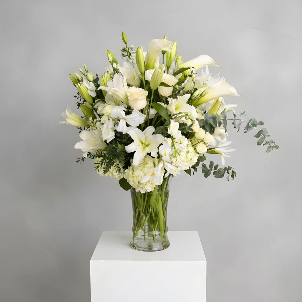 Eternal Grace Tribute - Elegant, serene, and timeless, Eternal Grace Tribute is a luxurious all-white arrangement featuring premium lilies, roses, calla lilies, hydrangea, snapdragons, and delicate seasonal blooms accented with fresh eucalyptus and lush greenery. Designed in a tall clear glass vase, this sophisticated piece conveys peace, purity, and heartfelt sentiment, making it ideal for sympathy services, memorials, churches, elegant events, or meaningful expressions of love and remembrance.