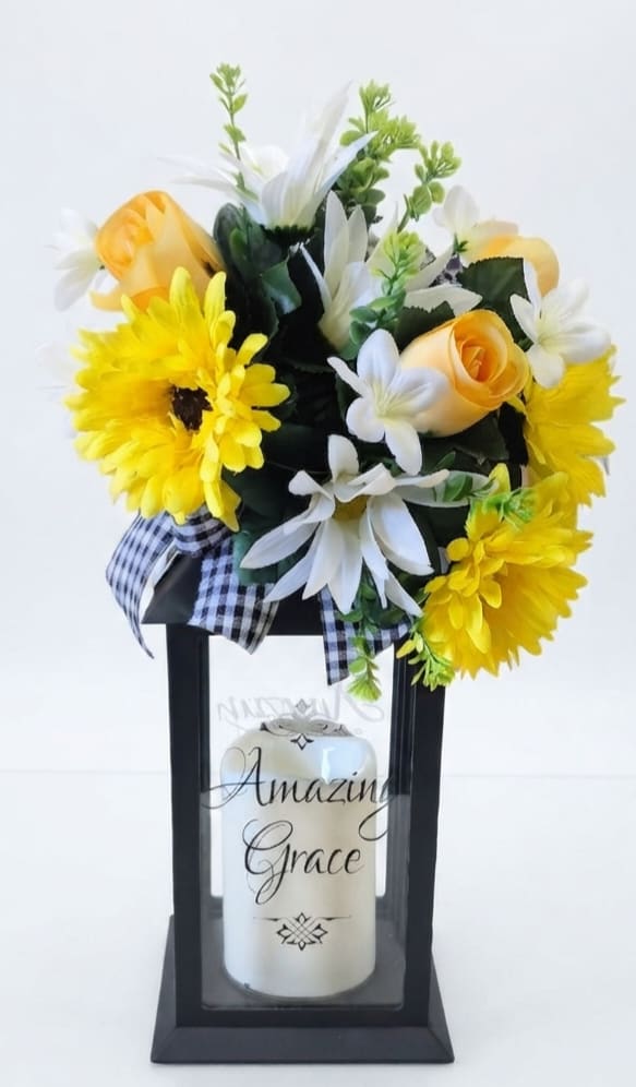 Yellow and white floral arrangement in a black lantern with a candle