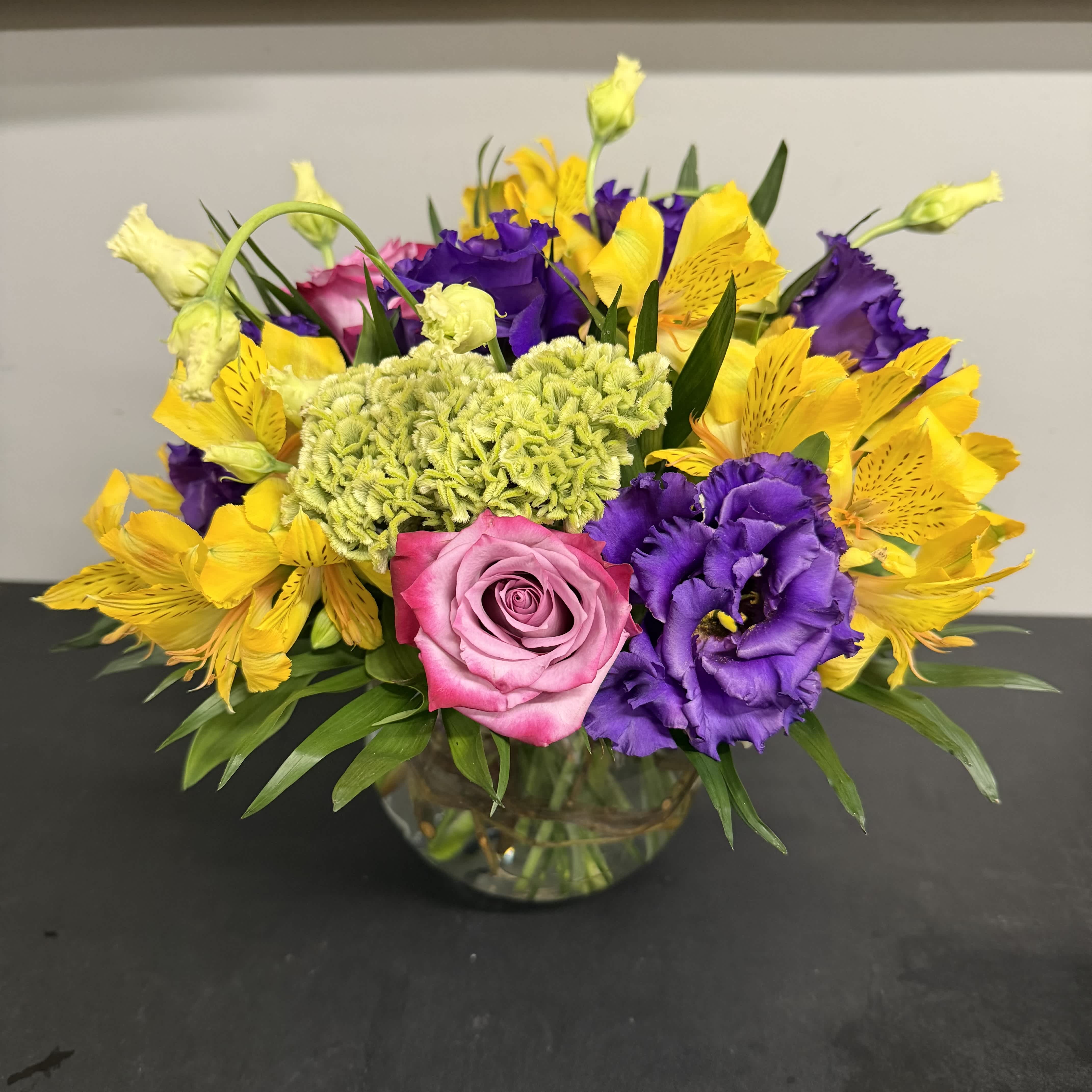 Mixed bouquet of pink, purple, and yellow flowers in a glass vase