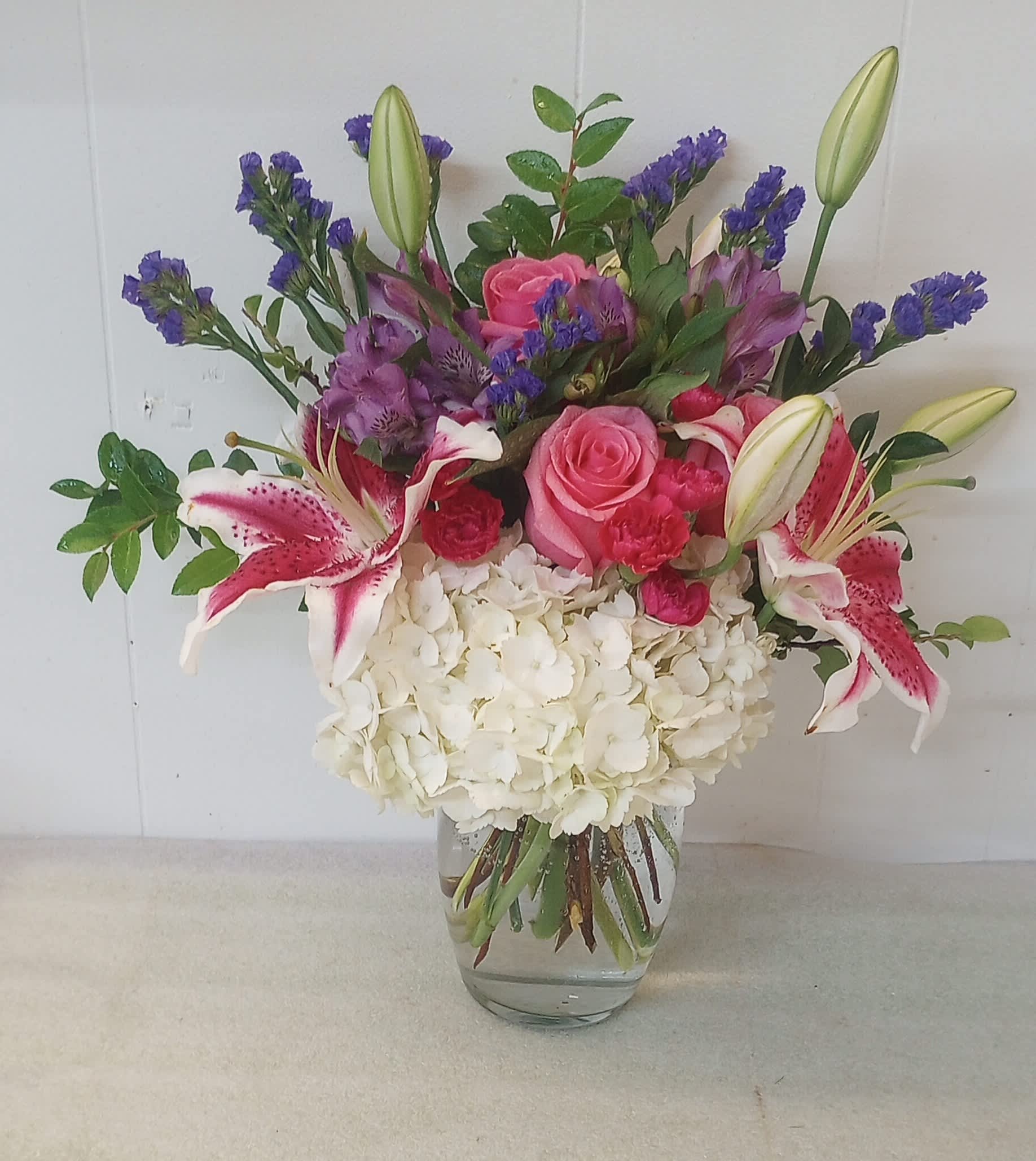 Mixed bouquet of pink roses, lilies, and white hydrangea in a glass vase