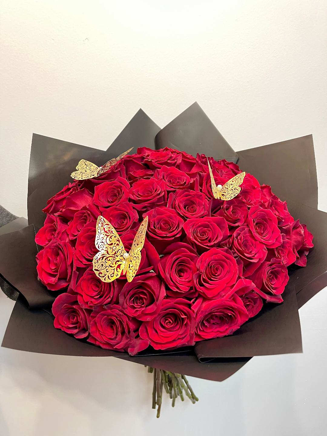 Bouquet of red roses wrapped in dark paper with gold butterfly accents