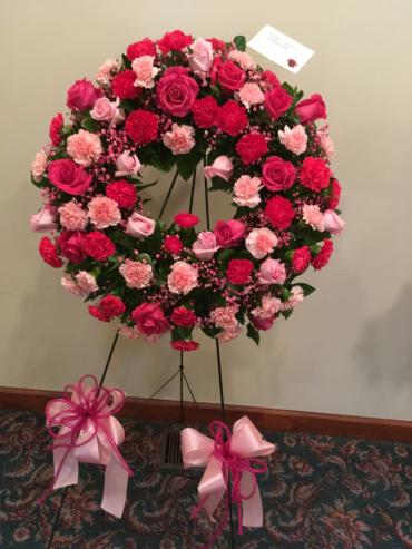 Pink and red floral wreath on a stand with ribbon bows