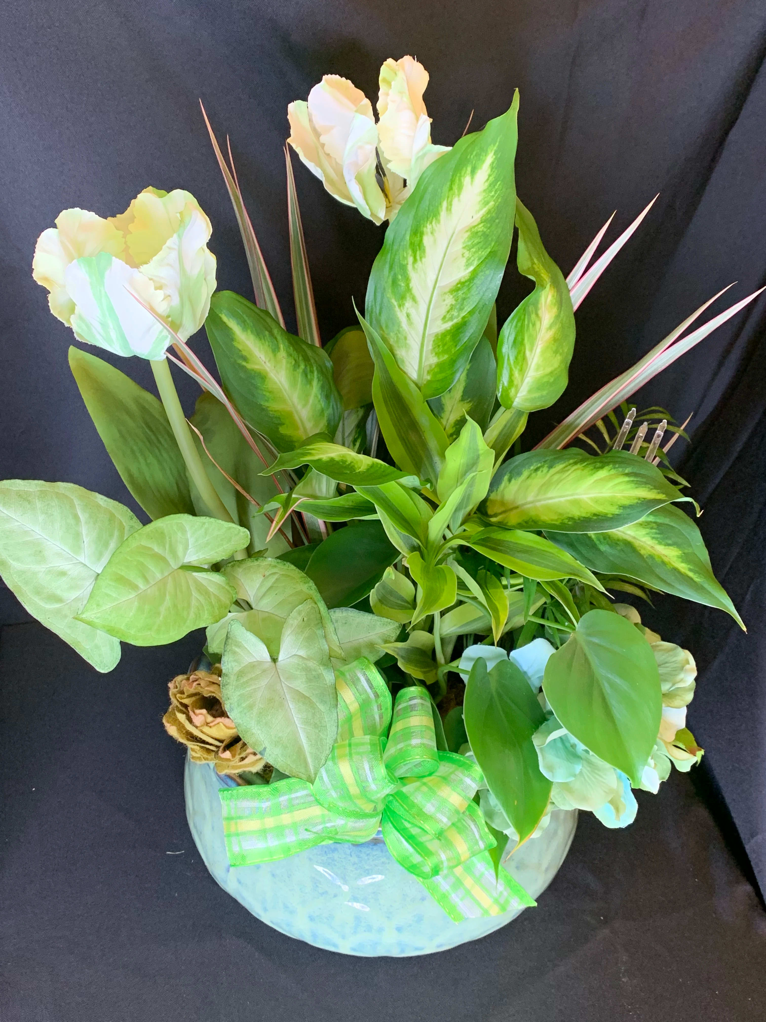Tropical arrangement with pale flowers and large variegated leaves in a round vase