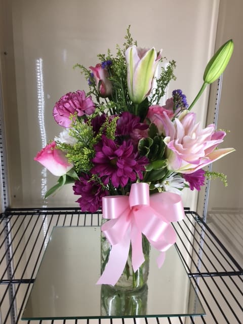Pink and purple flower arrangement in a glass vase with a pink ribbon