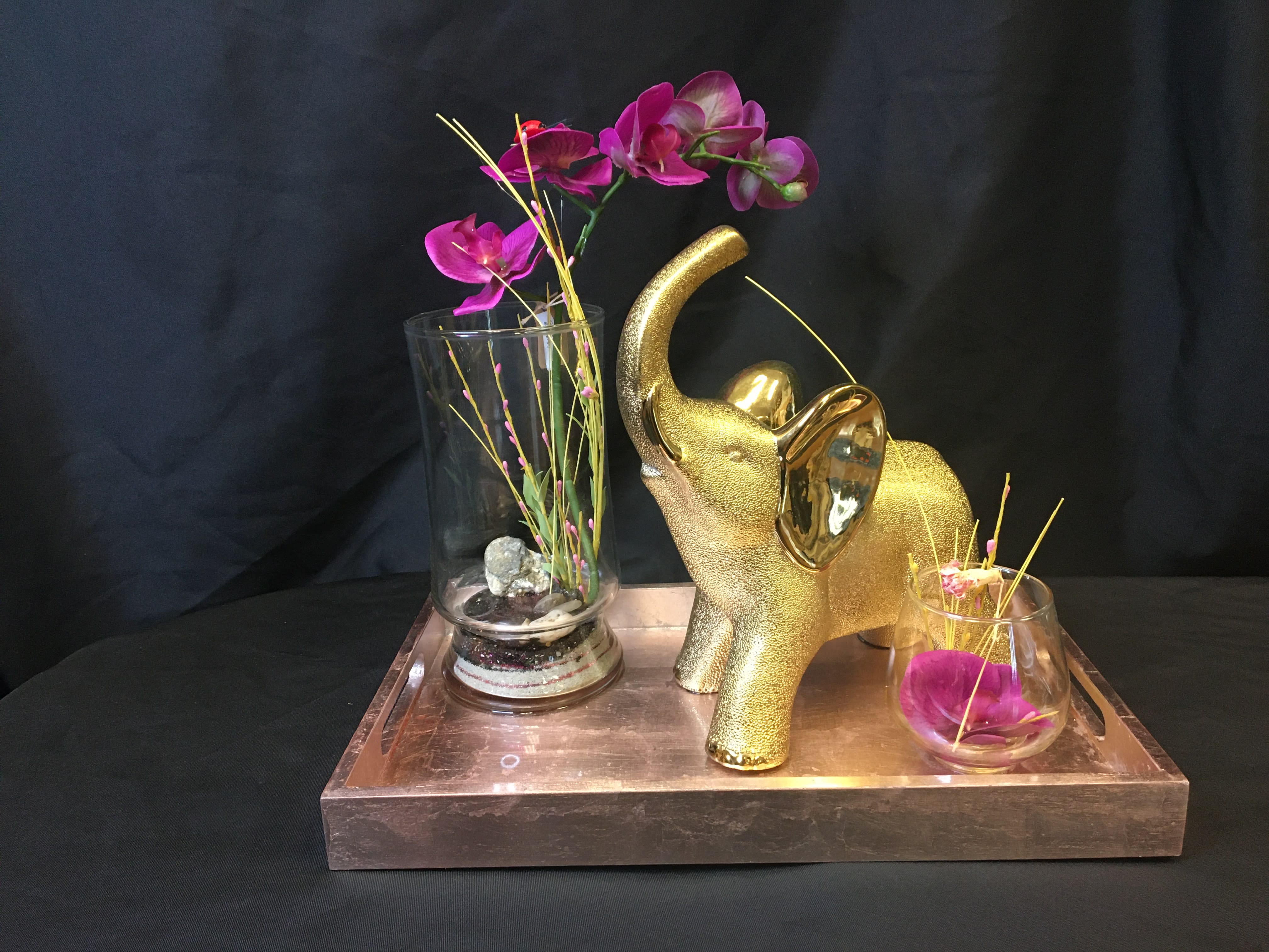 Gold elephant figurine with purple orchids in glass vases on a tray